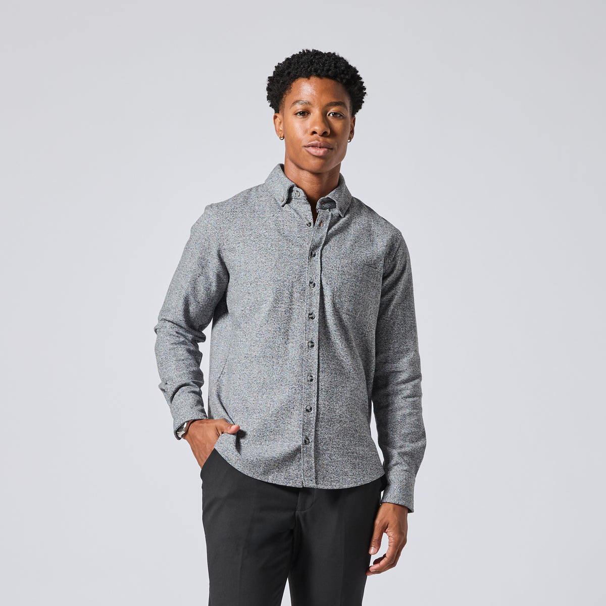 Model wearing a gray long-sleeve button-down shirt with a subtle textured pattern, paired with black trousers, standing against a light gray studio background. Color: Static