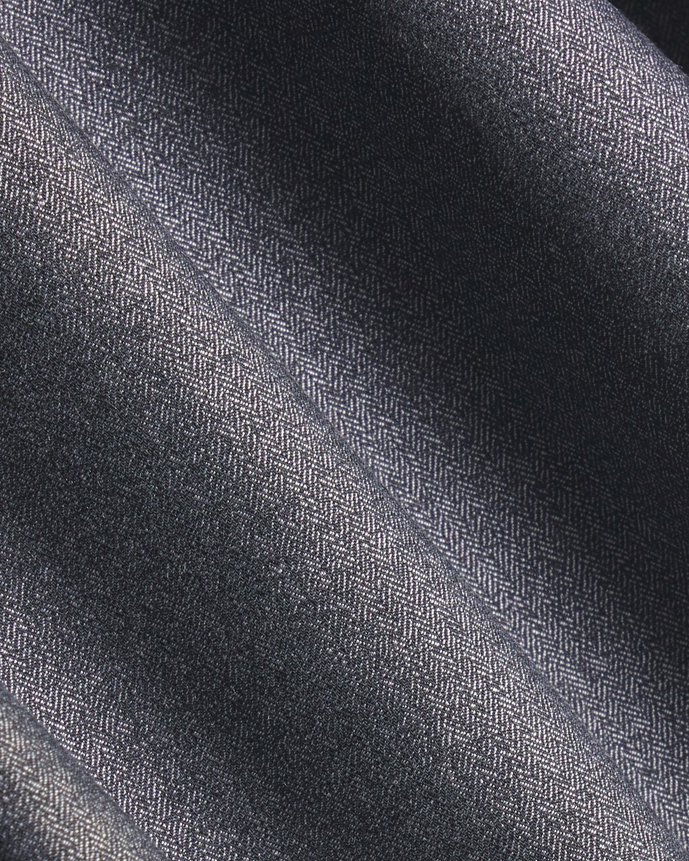 A close-up of dark charcoal gray herringbone fabric with a subtle woven texture and soft diagonal folds. Color: Steel Marl Herringbone