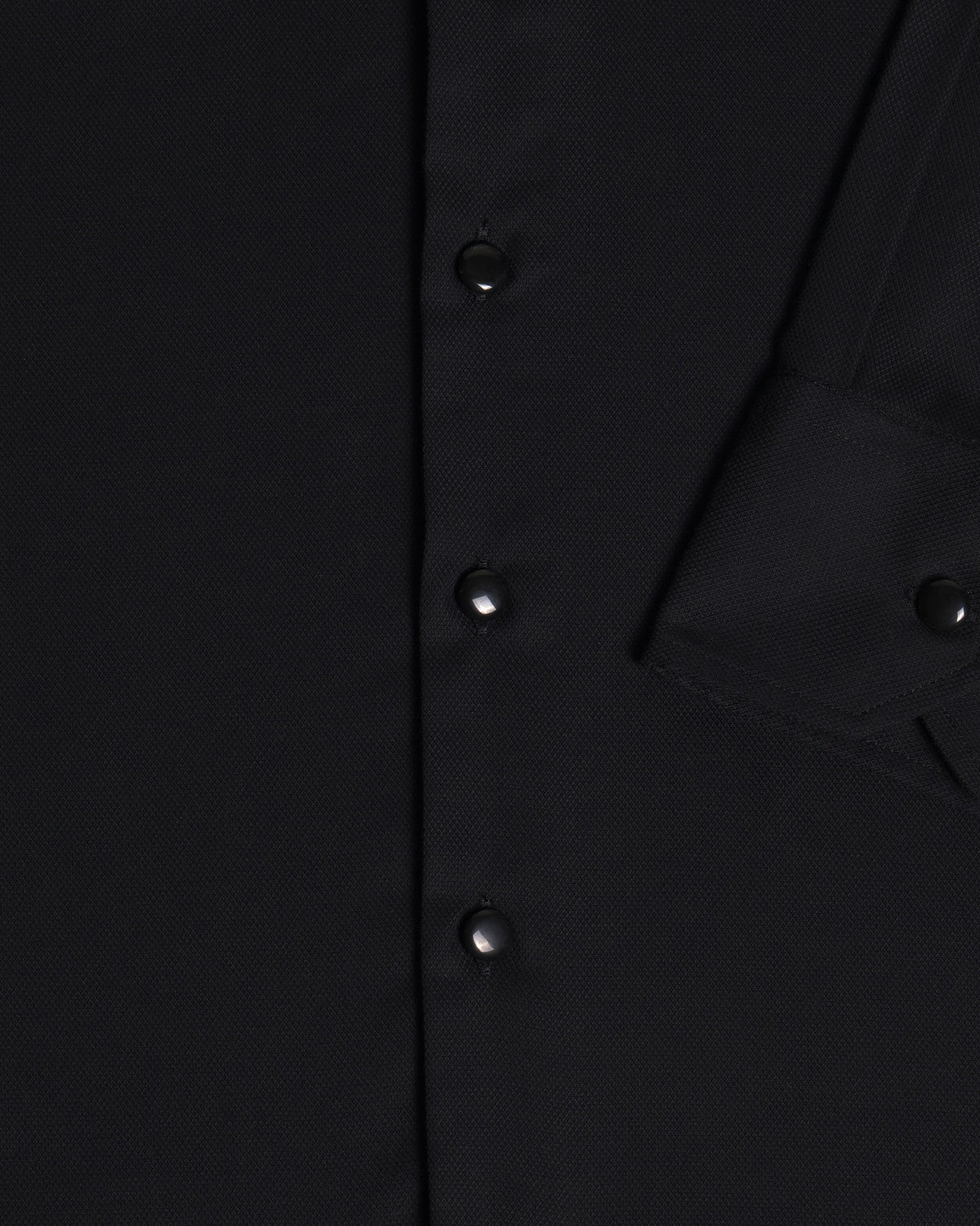 Close-up of a black button-front garment showing the fabric texture, a vertical button placket, and sleeve cuff. Color: Black