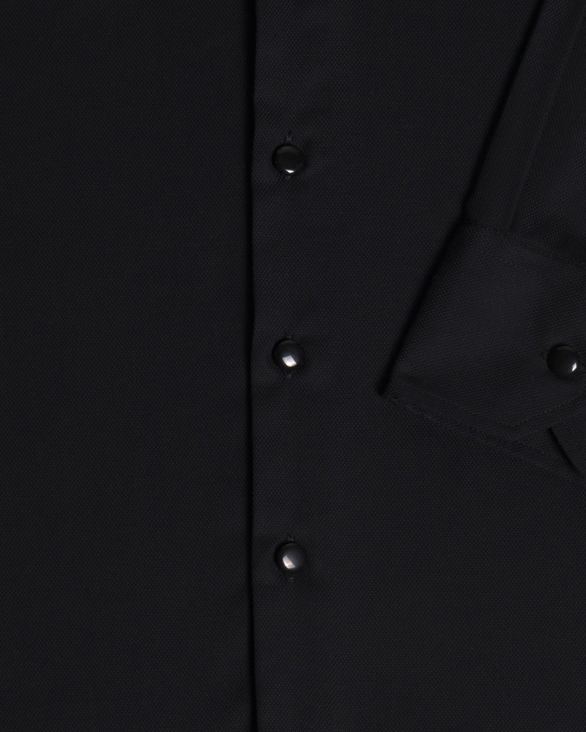 Close-up of a black button-front garment showing the fabric texture, a vertical button placket, and sleeve cuff. Color: Black