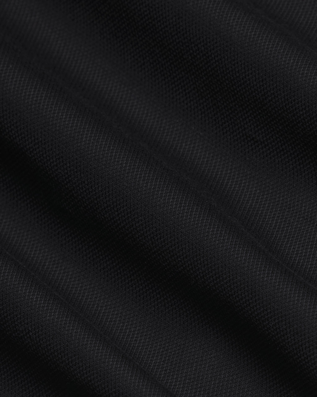 A close-up of black textured fabric with a fine woven pattern and soft diagonal folds. Color: Black
