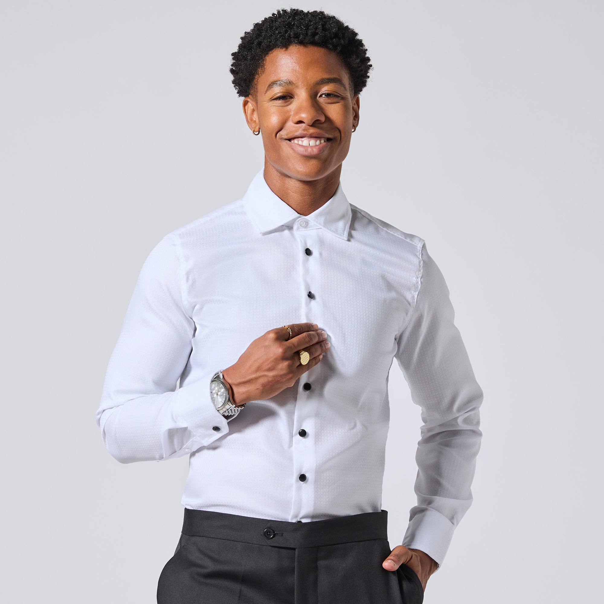 Model wearing a white long-sleeve dress shirt with black buttons and dark trousers, standing against a light gray studio background. Color: White Twill Grid