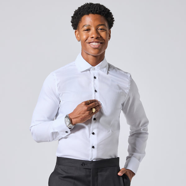 Model wearing a white long-sleeve dress shirt with black buttons and dark trousers, standing against a light gray studio background. Color: White Twill Grid
