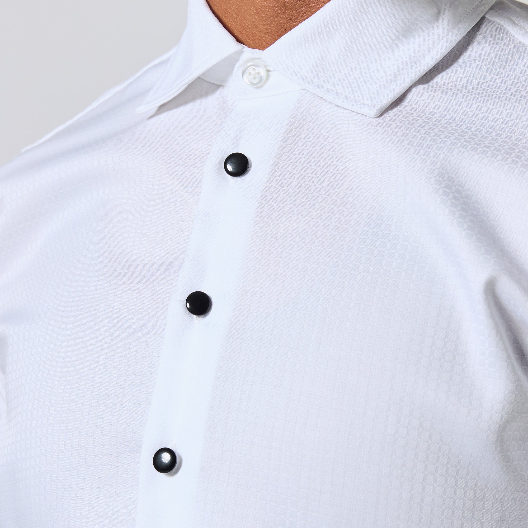 Close-up of a white long-sleeve button-down shirt with a subtle geometric pattern, featuring black buttons and a pointed collar. Color: White Twill Grid