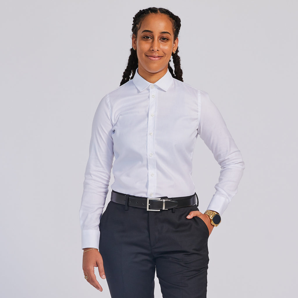 A person wearing a white easy-care dress shirt with a spread collar, white buttons, and long sleeves, paired with dark trousers and a belt.