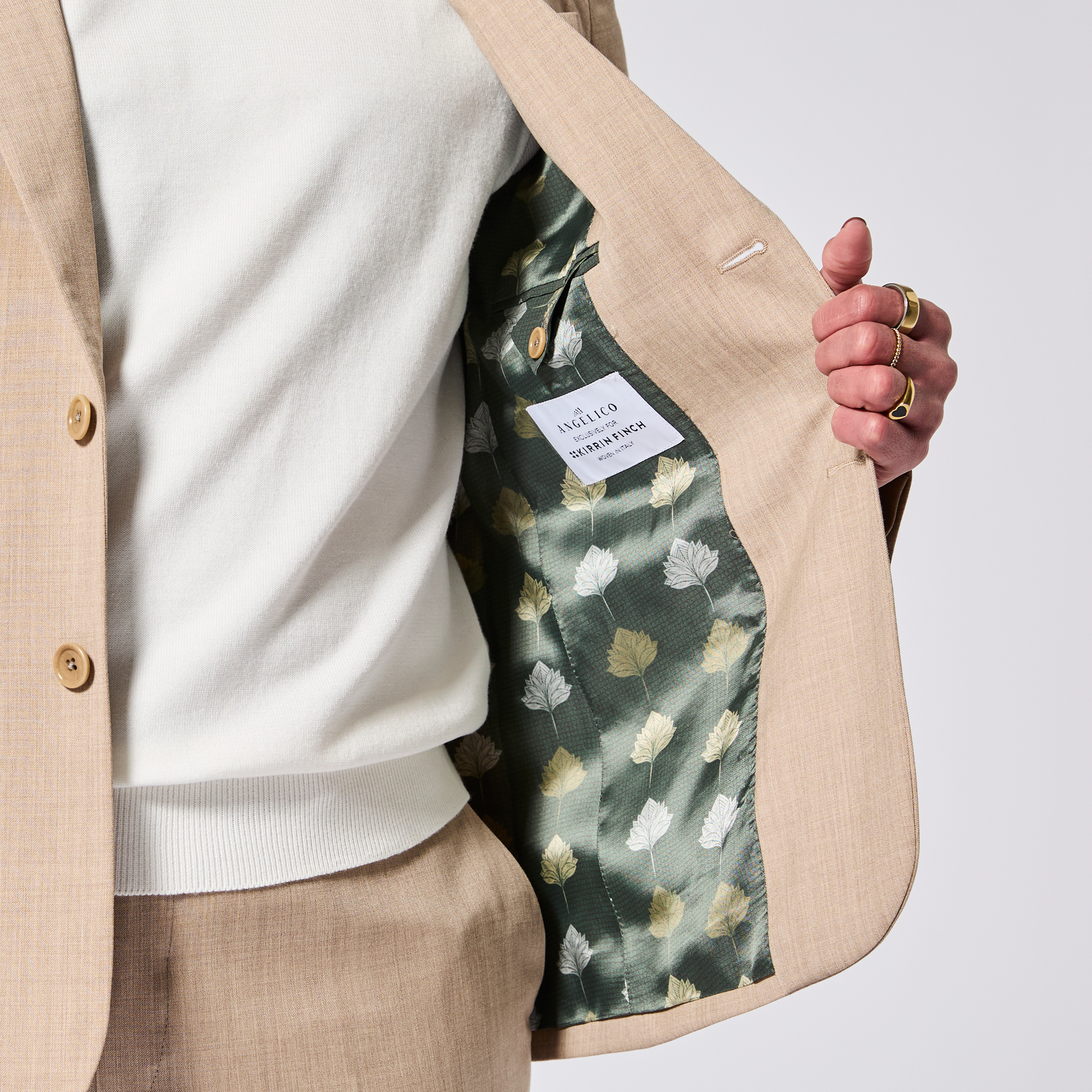 Person wearing a Georgie blazer with a white knit t-shirt, showing the blazer's lining, a patterned green garment with a repeated lotus flower. Color: Desert