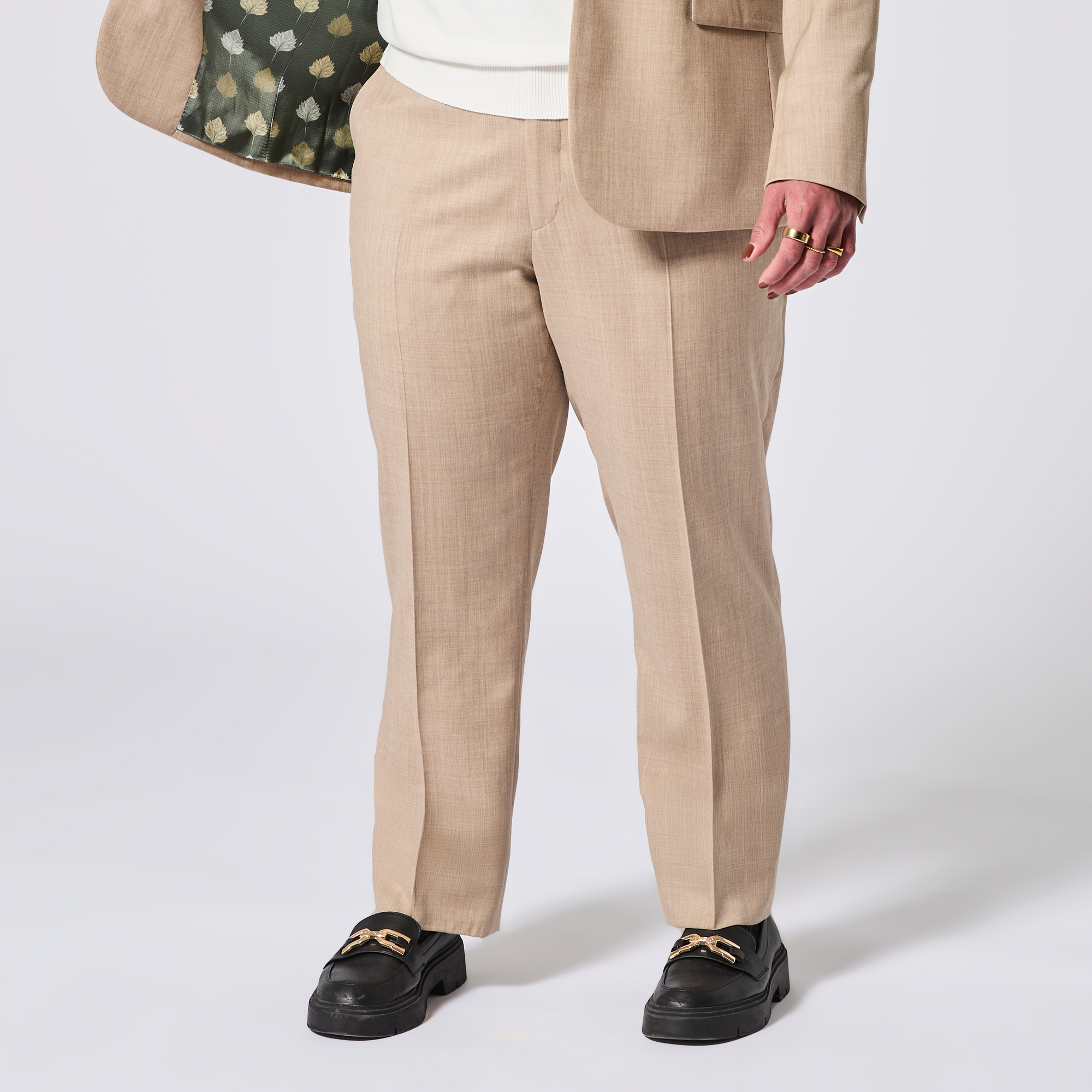 Person wearing beige suit pants and a blazer with a white background. Color: desert