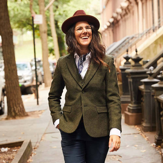 Model smiling and sauntering down a Brooklyn street wearing olive herringbone tweed blazer and vest by Kirrin Finch