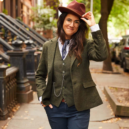 Model tipping their burgundy hat while wearing olive herringbone tweed blazer and vest by Kirrin Finch while walking down the street