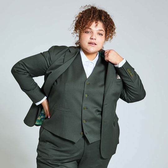 Model wearing the entire Georgie Olive suit by Kirrin Finch. Blazer, vest, and dress pants all made in Italy. A glimpse of gold leaf lining can be seen ad the model has swooped back the blazer to place hand above their hip.