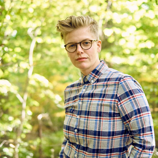 Androgynous model wearing brushed flannel plaid outdoors, leafy green background