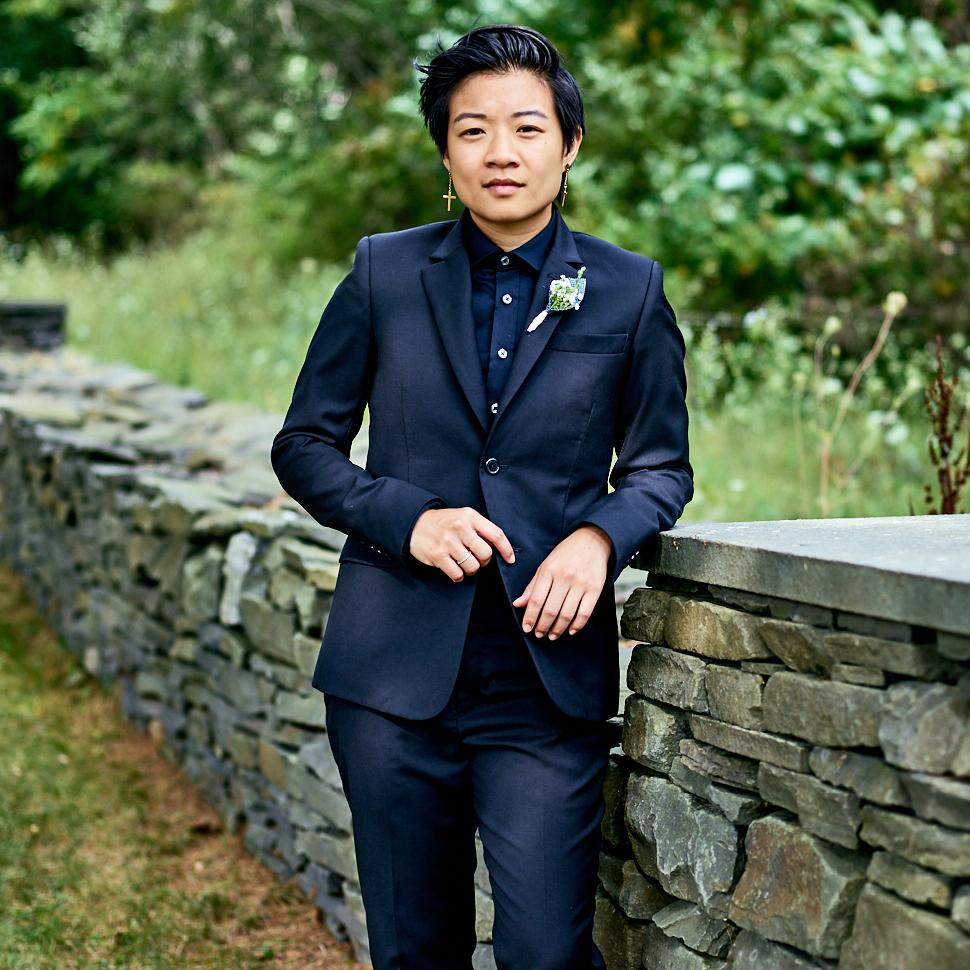 Model posed posed by stone fence wearing all black Kirrin Finch suit