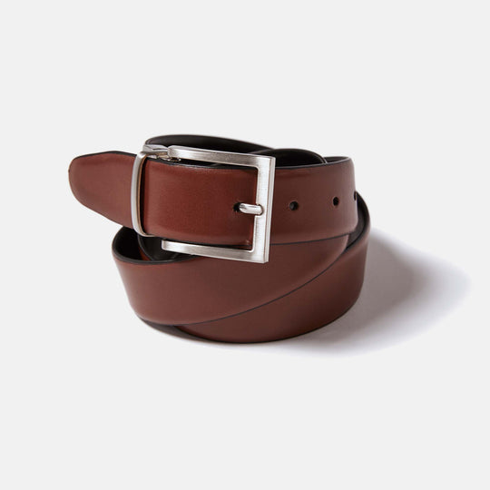 Reversible leather belt by Kirrin Finch coiled upon itself. Showing brown leather side and zinc belt buckle. 