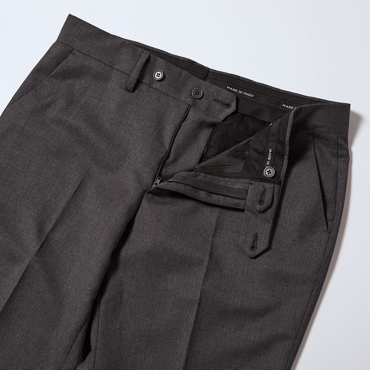 The Georgie Charcoal Dress Pants flat showing interior waistband. Made in intake is stitched into this wasitband several times. Waist has double button enclosures also in charcoal. Color: Charcoal