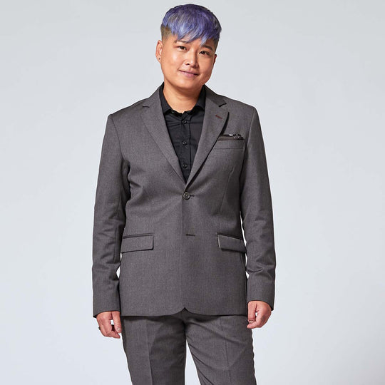 Androgynous model wearing charcoal blazer over black classic dress shirt and matching charcoal dress pants with deep pockets