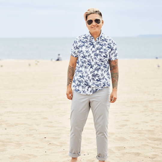 Androgynous model wearing deep pocket gray chinos on the breach with a palm tree pattern short sleeve shirt