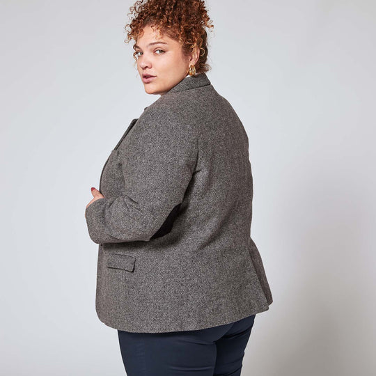 Model shot 3/4 from behind in gray tweed blazer in size 3XL looking over her shoulder. The shot also exposes the black faux suede elbow patch