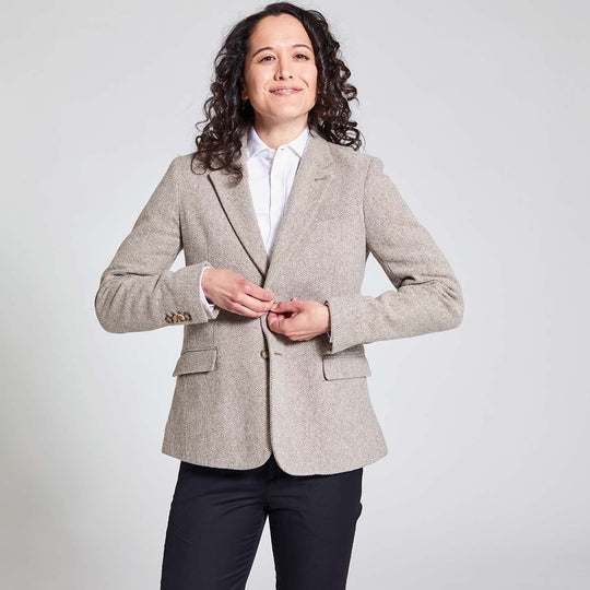 Dapper model wearing a menswear inspired taupe tweed herringbone blazer. She is clasping the top blazer button closed.
