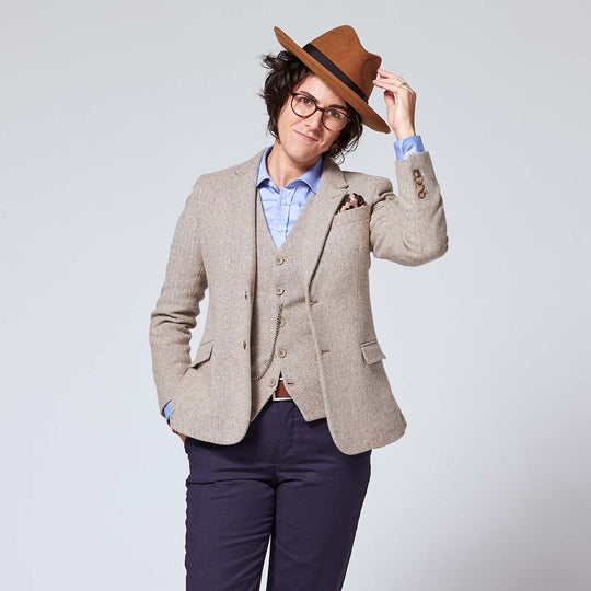 Non-binary model tipping their hat while wearing Taupe Tweed Blazer and vest underneath.