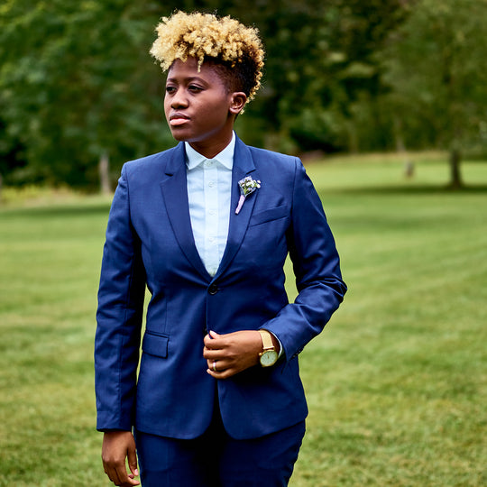 Model with blonde afro mohawk posing in formal dark blue suit on outside grounds